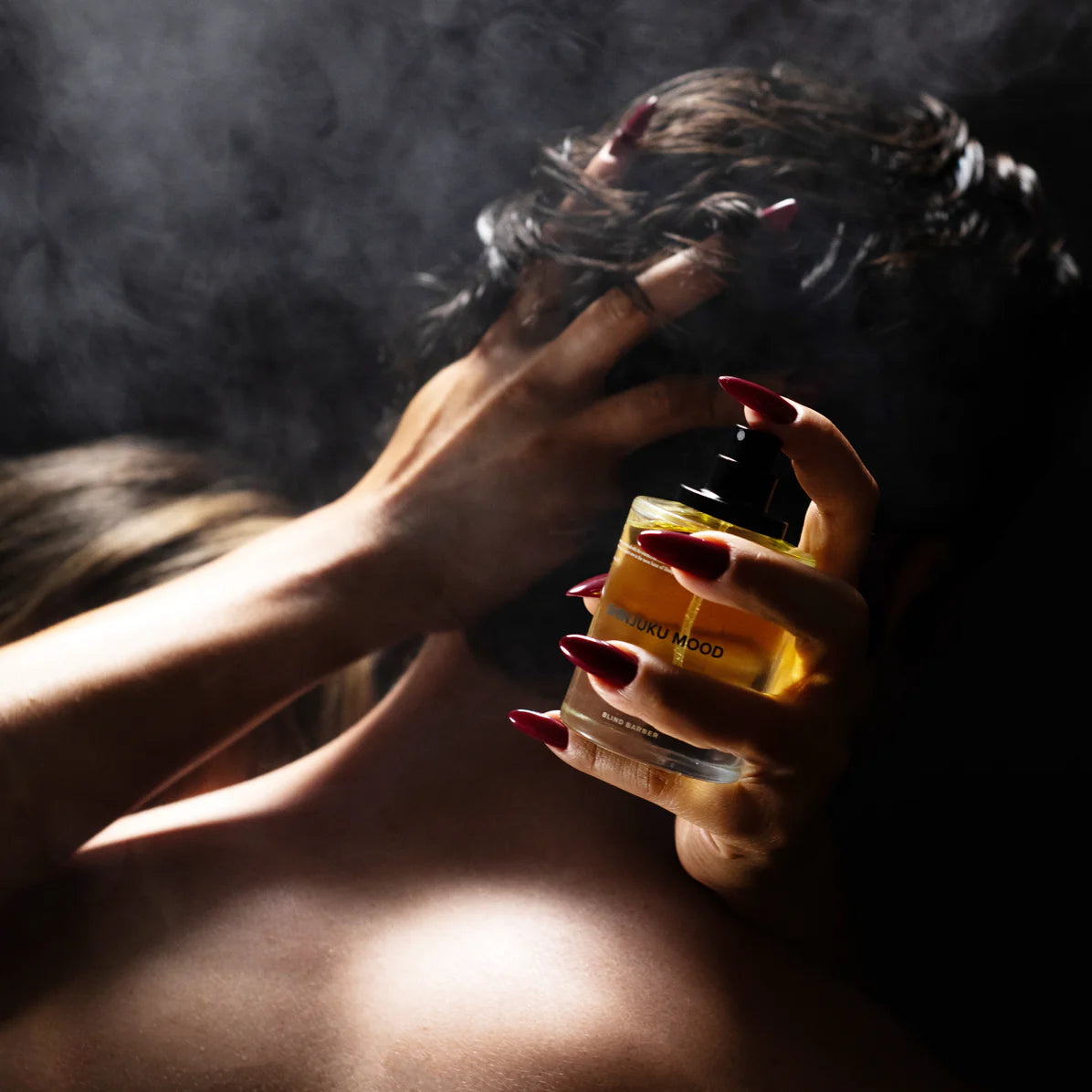 Hand holding a perfume bottle with smoke in the background