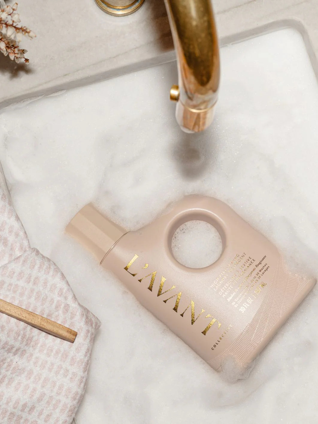 Pink bottle with gold text on a white surface, likely a product from the brand 'L'AVANT'.