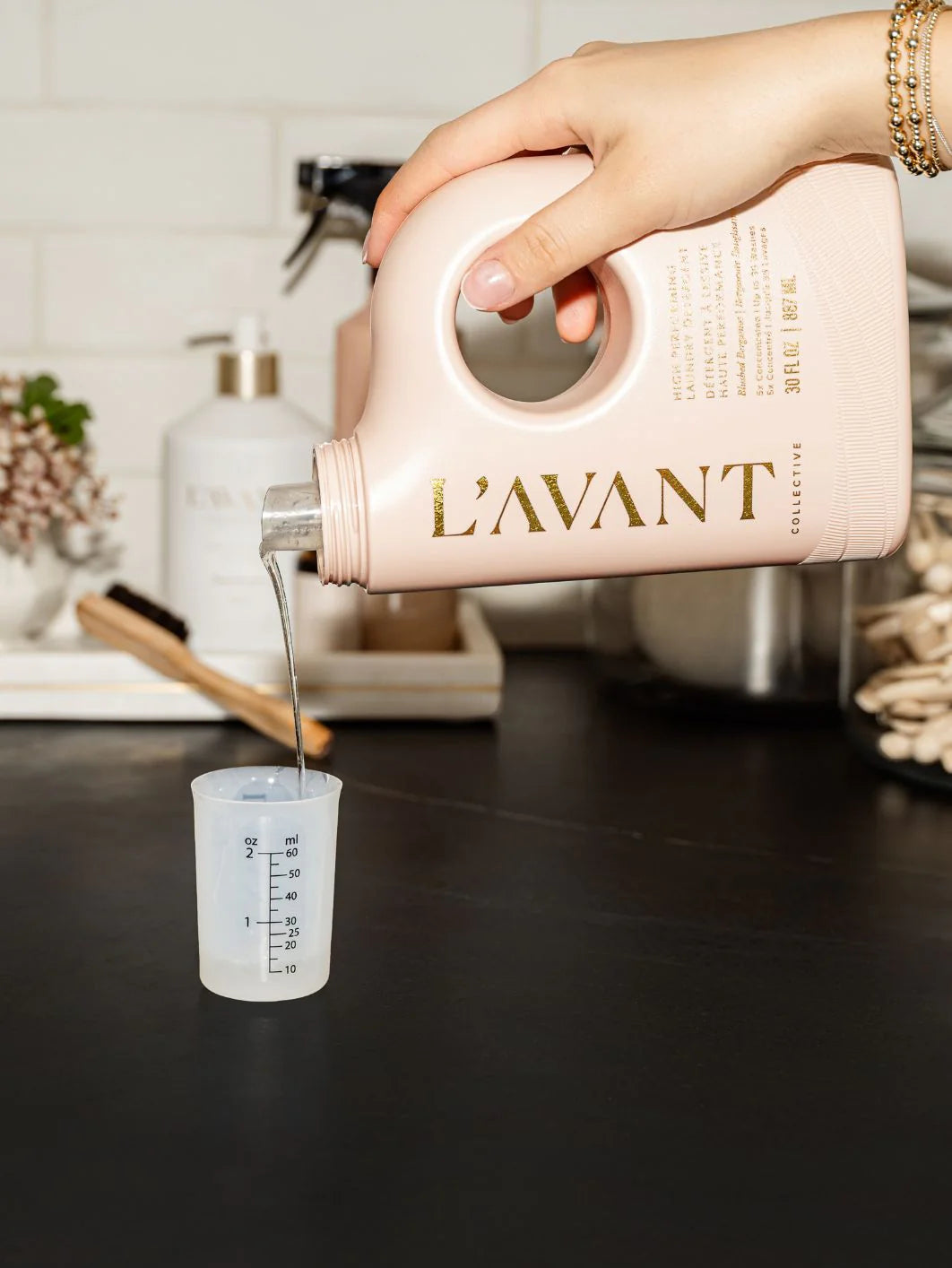 Person pouring liquid from a 'L'AVANT' container into a measuring cup on a kitchen counter.
