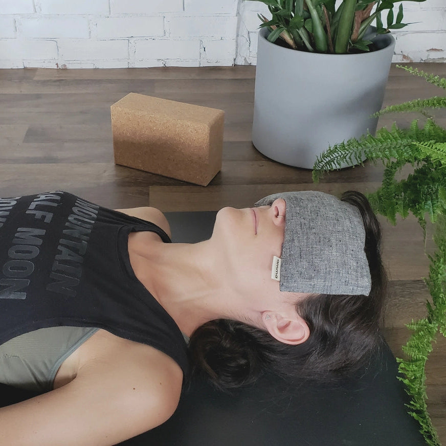 Person lying on a yoga mat with a headband, surrounded by plants indoors.