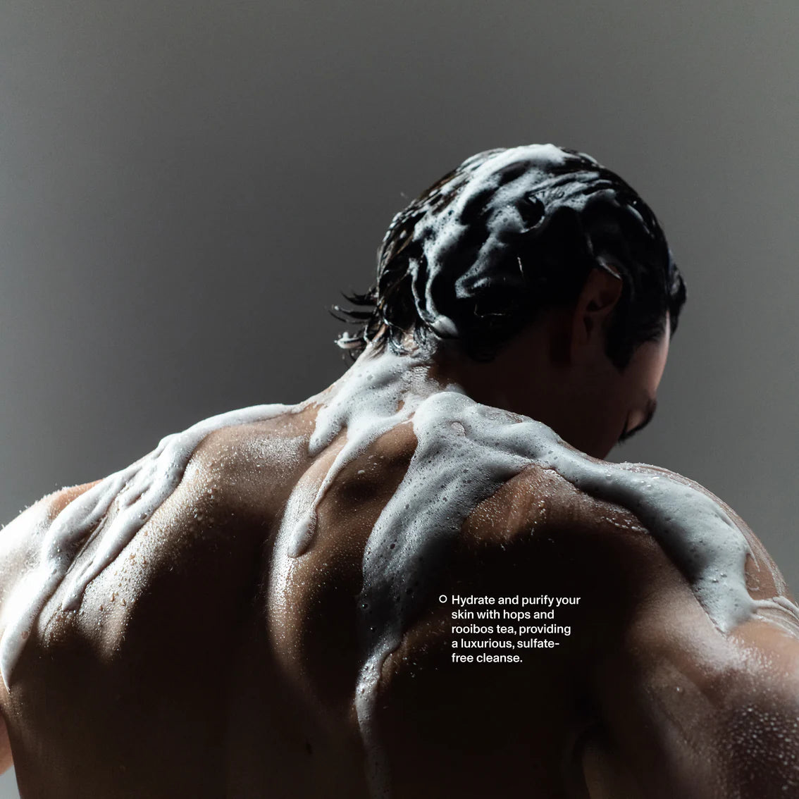 Person with soap suds on their back against a dark background