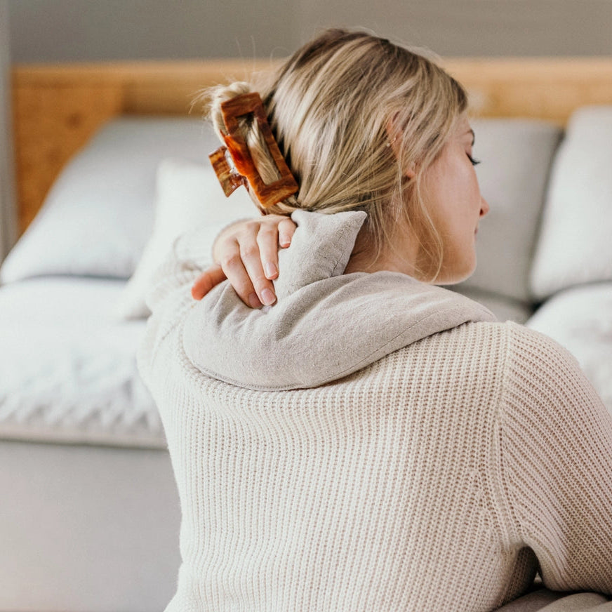 Woman sitting on a couch using aneck heating pad in a cozy living room.