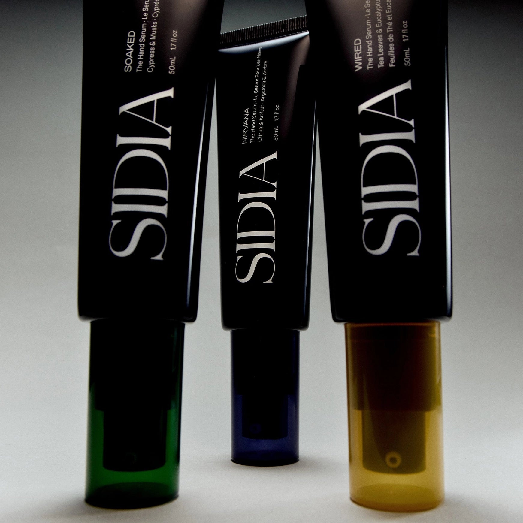 Three Sidia hand care products with different colored bottles on a gray background