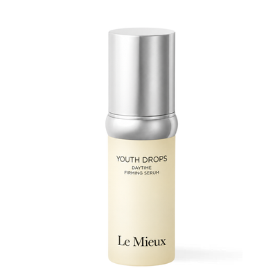 Le Mieux Youth Drops Daytime Firming Serum in a cylindrical bottle with a cream-colored body and a metallic silver cap, shown on a plain white background.