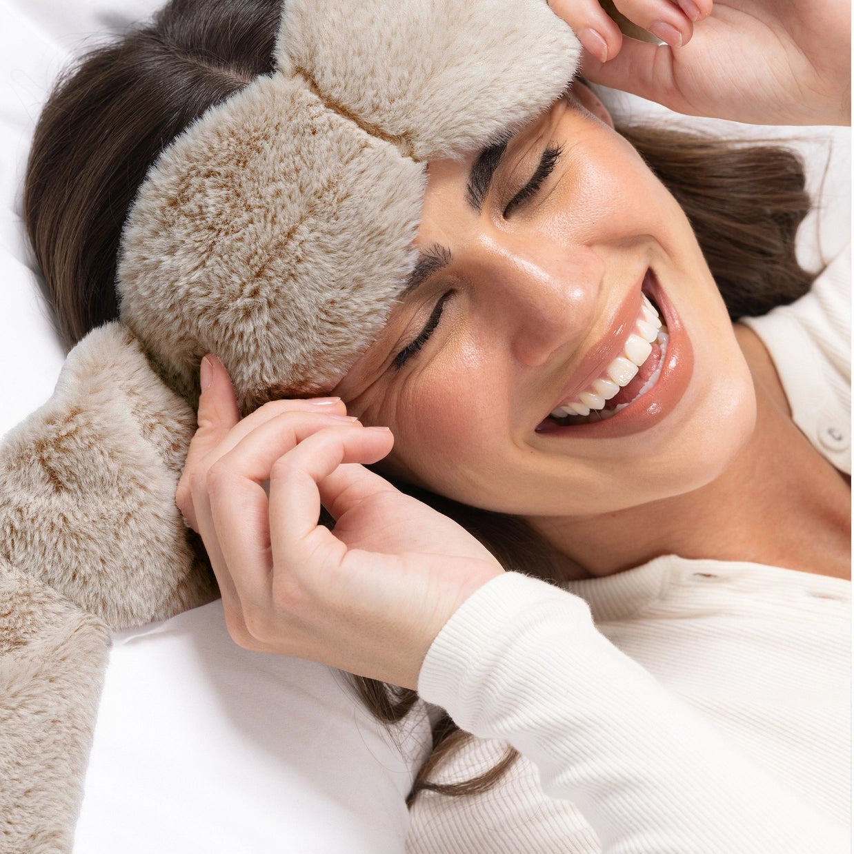 Woman wearing fluffy eye masks and a white shirt, smiling.