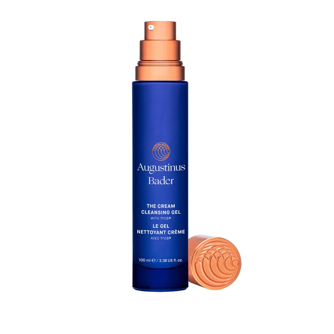 Augustinus Bader The Cream Cleansing Gel in a 500 ml dark blue bottle with a metallic copper pump, shown next to its matching copper cap on a white background.
