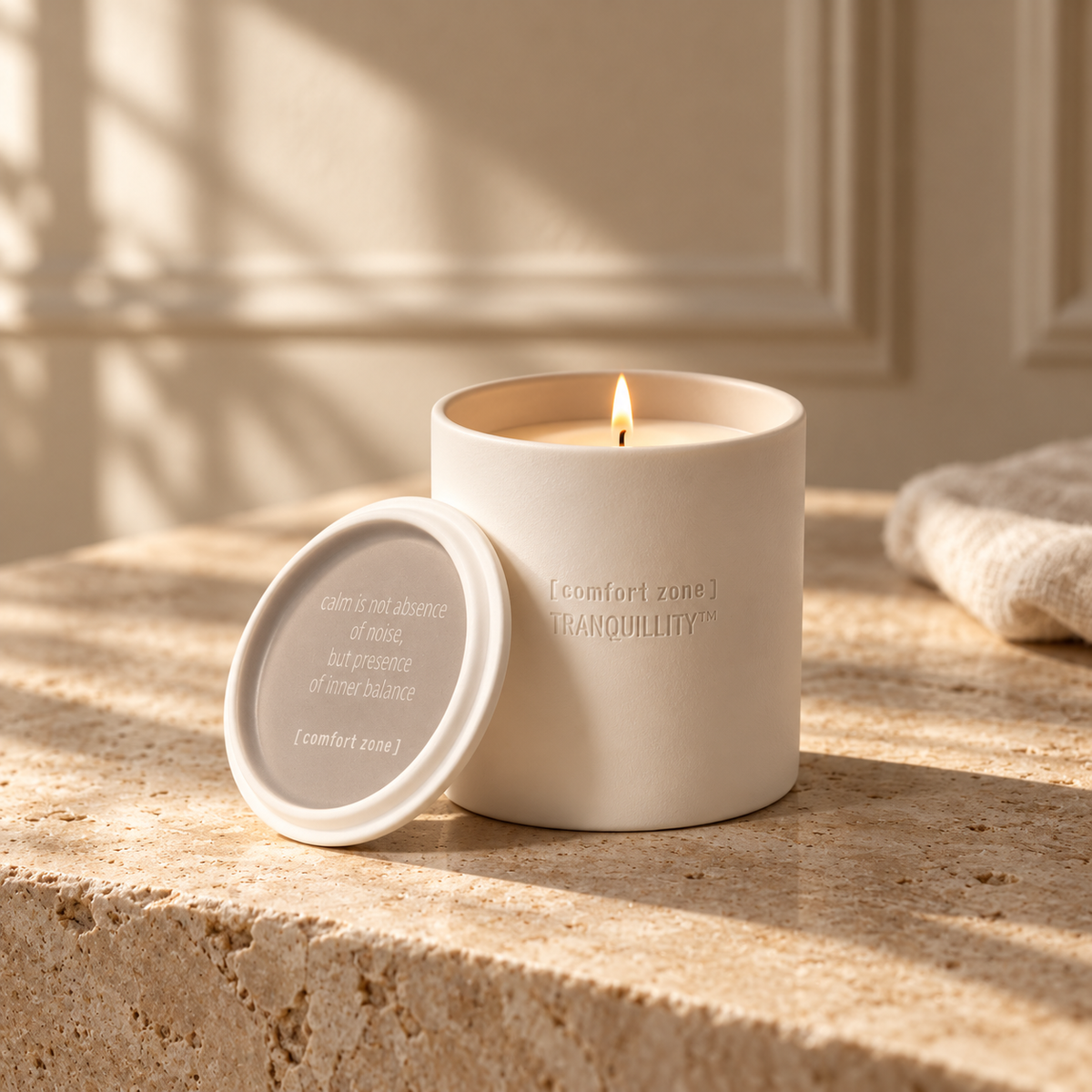 Holiday Tranquillity ceramic candle burning on warm limestone in a softly lit beige interior