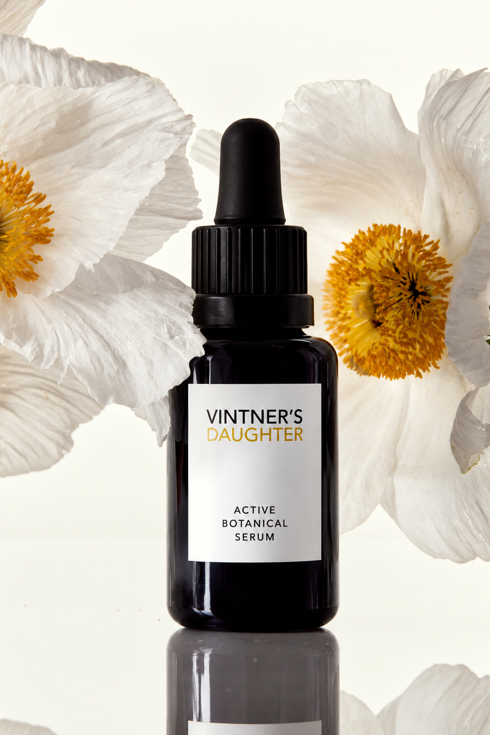 Vintner’s Daughter Active Botanical Serum facial oil in a dark dropper bottle surrounded by white flowers with golden centres.